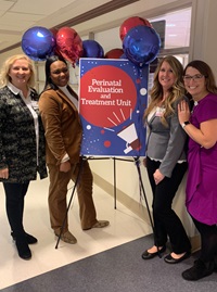 Four PETU employees stand next to a poster displaying “Perinatal Evaluation and Treatment Unit” with red and blue balloons attached